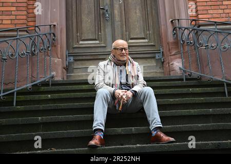 Wiesbaden, Deutschland. 17. Mai 2023. Direktor Volker Schlöndorff sitzt vor Beginn einer Pressekonferenz für die Ausstellung „Volker Schlöndorff. Von Wiesbaden in die Welt' auf einer Treppe der Marktkirche. Die Ausstellung auf der FilmBühne Caligari zeigt Publikationen und Filmserien über das Leben und Werk des preisgekrönten Filmemachers vom 19. Mai bis 18. Juni 2023. Kredit: Arne Dedert/dpa/Alamy Live News Stockfoto