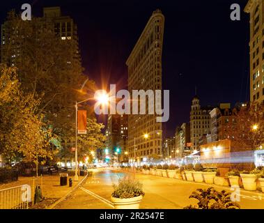 Das Flatiron Building leuchtet warm unter Straßenlaternen unter einem indigo-Himmel vor der Morgendämmerung. Der schwache Verkehr hinterlässt leichte Wege bei zeitlicher Belichtung. Stockfoto