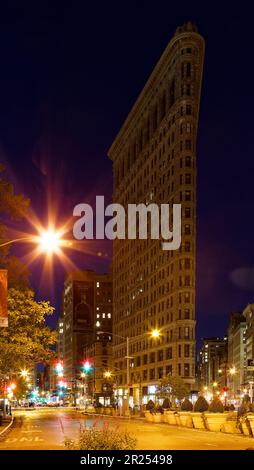 Das Flatiron Building leuchtet warm unter Straßenlaternen unter einem indigo-Himmel vor der Morgendämmerung. Der schwache Verkehr hinterlässt leichte Wege bei zeitlicher Belichtung. Stockfoto