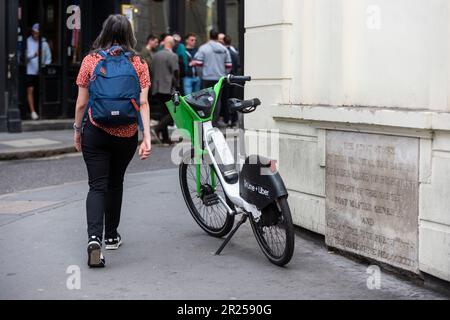 London, Großbritannien. 17. Mai 2023 Die Frau überholt ein elektrisches Mietrad auf einem Bürgersteig in Covent Garden im West End. Im Gegensatz zum Fahrradverleihsystem von Santander, das Fahrradparkplätze vorsieht, verfügen Unternehmen, die die elektrischen Mietzyklen anbieten, wie Lime von Uber, Human Forest und dott, nicht über solche Parkbuchten. Es wurde berichtet, dass Westminster Council Pläne ausarbeitet, um Fahrern, die ihre gemieteten Fahrräder nicht ordnungsgemäß parken, Geldstrafen zu zahlen, und dass Leihfahrräder, die auf Gehwegen zurückgelassen werden, eine Gefahr für Fußgänger und Rollstuhlfahrer darstellen können. Kredit: Stephen Chung / Alamy Live News Stockfoto