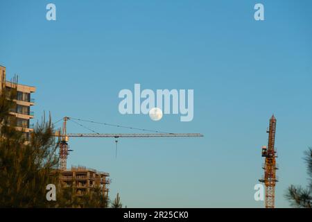 Baukräne, Teil eines Gebäudes, das gegen den Himmel gebaut wird, mit einem großen Mond Stockfoto