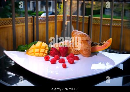 Wunderschönes leckeres Dessert auf einem riesigen quadratischen weißen Teller auf dem Balkon des privaten Hauses, tropische Früchte Croissants, traditionelles französisches Mittagessen, köstliches Frühstück, das wunderschöne Speisen serviert Stockfoto