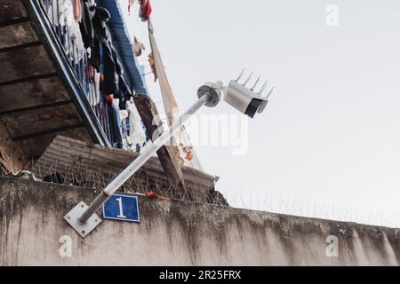 Lissabon; Low-Angle-Aufnahme einer weißen Sicherheitskamera, die an einem sehr alten und schmutzigen Gebäude an einem klaren Himmel in einem bescheidenen Nachbarn befestigt ist Stockfoto