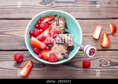 Süßes Schokoladeneis in der Schüssel auf rustikalem Holzhintergrund mit Scheiben frischer Erdbeeren und flachem Boden Stockfoto