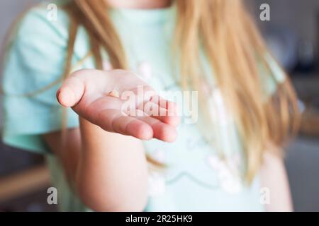 Die Hand eines kleinen Mädchens hält sie und zeigt ihren Milchzahn aus der Nähe. Das Milchzahnverlustkonzept Stockfoto