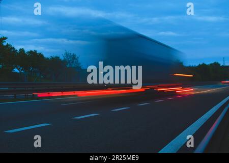 Ein Lkw, der mit hoher Geschwindigkeit auf der Autobahn fährt. Bewegungsunschärfe auf der Autobahn. Autobahnlichter. Konzept des internationalen Transports und der Logistik Stockfoto