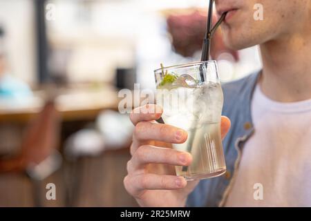 Der Mann trinkt Limonade oder Kokosschwanz durch einen Strohhalm aus Glas mit Eis. Stockfoto