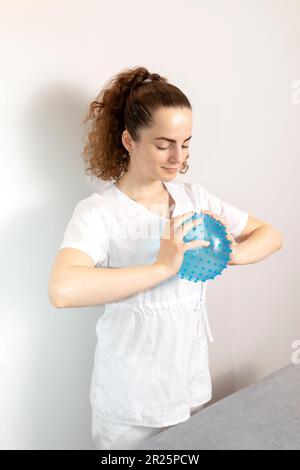 Kaukasischer Rehabilitationsspezialist, Physiotherapeut In Weißer Medizinischer Kleidung Hält Massageball Mit Pickel Im Therapiekabinett. Gesundheit Stockfoto