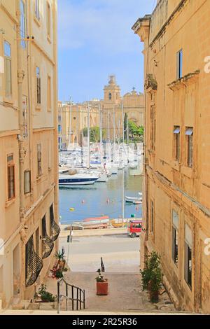 Foto wurde auf der Insel Malta aufgenommen. Das Bild zeigt eine kleine Straße der Küstenstadt Senglea mit Blick auf den Hafen und befestigten Yachten. Stockfoto