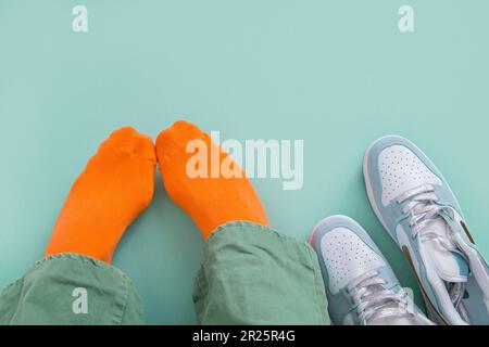 Die Füße eines Mannes in orangefarbenen Socken mit seinen Turnschuhen ziehen ab. Mintgrüner Hintergrund Stockfoto