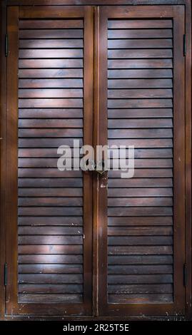 Holztür mit Lamellenbelüftung, Sonnenschutzrollos Tür mit Vorhängeschloss geschlossen, Nahaufnahme, vertikaler Rahmen. Stockfoto