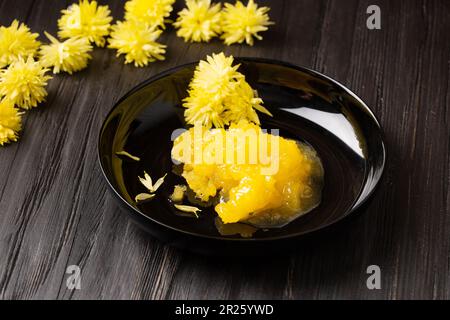 Kristallisierter Honig auf einem schwarzen runden Teller und gelbe Blumen auf dunklem Holzhintergrund. Stockfoto