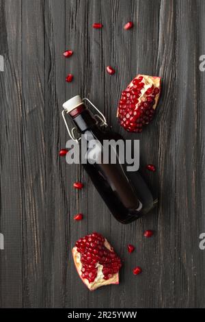 Reifer Granatapfel, verstreute große Körner, frisch gepresster Granatapfelsaft in einer transparenten Flasche auf einem hölzernen Hintergrund von oben. Stockfoto