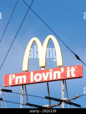 McDonalds Logo und -Schild, wie durch Überlandleitungen oder Straßenbahnkabel in der Stadt gesehen Stockfoto