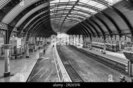 Ein Panorama einer Station mit einem geschwungenen Baldachin aus dem 19. Jahrhundert. Ein Zug wartet auf einem Nebengleis, und im Vordergrund befinden sich Signalleuchten. Die Passagiere warten auf der Pl Stockfoto