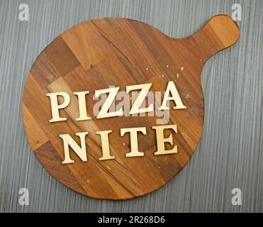 Runde Pizzabrette aus dunklem Holz mit Krümeln auf Tischdecken. Das Wort "Pizza-Abend", das an Bord geschrieben wird Stockfoto