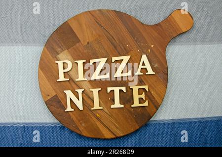 Runde Pizzabrette aus dunklem Holz mit Krümeln auf Tischdecken. Das Wort "Pizza-Abend", das an Bord geschrieben wird Stockfoto