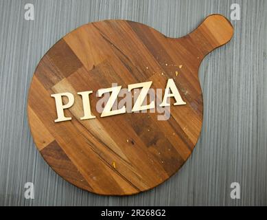 Runde Pizzabrette aus dunklem Holz mit Krümeln auf Tischdecken. Das Wort Pizza, das an Bord geschrieben wurde Stockfoto