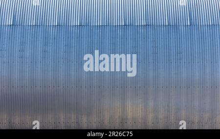 Glänzend gebogene, gerippte Metallwand eines Lagergebäudes, moderne industrielle Architektur im Hintergrund Fotostruktur Stockfoto