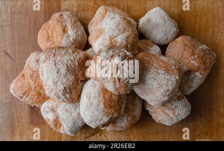 Ein Haufen frisch gebackener, weißer, verkrusteter, hausgemachter Ciabatta-Rollen auf einem rustikalen Holztisch, Draufsicht, Seitenansicht. Stockfoto