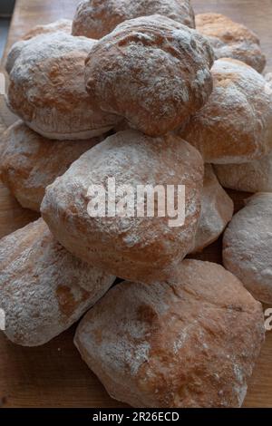 Ein Haufen frisch gebackener, weißer, krustender, hausgemachter Ciabatta-Rollen auf einem rustikalen Holztisch, Draufsicht, Seitenansicht. Stockfoto