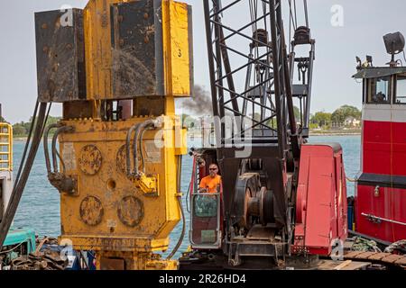 Detroit, Michigan: Die Arbeiter reparieren die Mauer entlang des Detroit Riverwalk mit einem Haufenfahrer, der auf einem Kahn am Detroit River montiert ist. Stockfoto