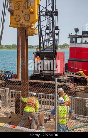 Detroit, Michigan: Die Arbeiter reparieren die Mauer entlang des Detroit Riverwalk mit einem Haufenfahrer, der auf einem Kahn am Detroit River montiert ist. Stockfoto