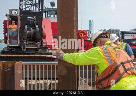 Detroit, Michigan: Die Arbeiter reparieren die Mauer entlang des Detroit Riverwalk mit einem Haufenfahrer, der auf einem Kahn am Detroit River montiert ist. Stockfoto