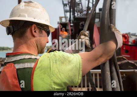 Detroit, Michigan: Die Arbeiter reparieren die Mauer entlang des Detroit Riverwalk mit einem Haufenfahrer, der auf einem Kahn am Detroit River montiert ist. Stockfoto