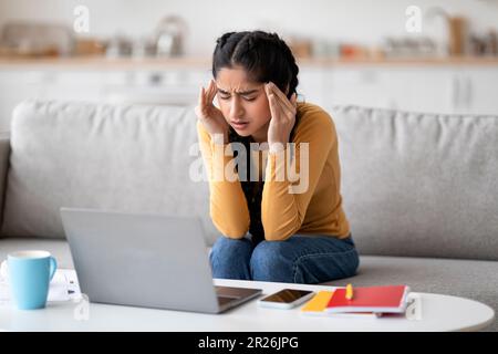 Freiberuflicher Stress. Indische Frau, Die Kopfschmerzen Hat, Während Sie Zu Hause Mit Einem Notebook Arbeitet Stockfoto