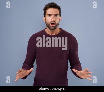 Warte, was? Studioaufnahme eines gutaussehenden jungen Mannes, der wütend vor grauem Hintergrund aussieht. Stockfoto