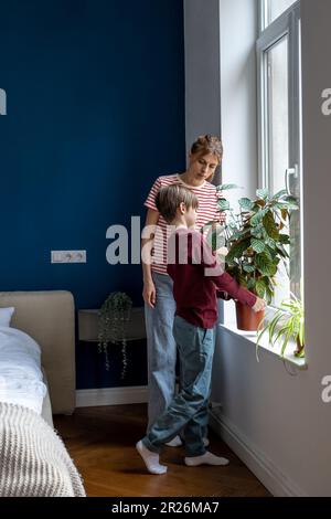 Aufmerksamer Sohn Junge, der Hausarbeiten macht, mit mutter, die sich um grüne Pflanzen kümmert. Zeit für die Familie. Stockfoto
