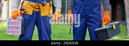 Ausgeschnittene Aufnahme von zwei männlichen Bauherren in blauen Overalls mit Werkzeugkasten auf der Baustelle Stockfoto