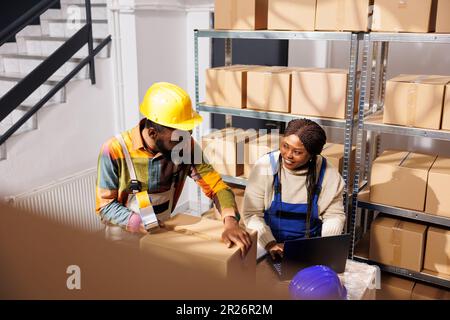 Mitarbeiter im Vertriebszentrum prüfen den Warenbestand auf einem Laptop Stockfoto