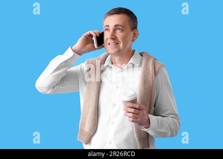 Ein erwachsener Mann mit einer Tasse Kaffee, der über ein Mobiltelefon auf blauem Hintergrund spricht Stockfoto