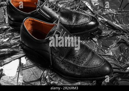 Stylische klassische Männerschuhe mit Wassertropfen auf schwarzem Hintergrund Stockfoto