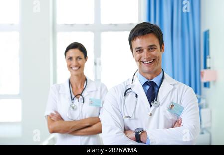 Legen Sie Ihr Leben in ihre Hände. Porträt eines gutaussehenden jungen Arztes mit seiner Pflegehelferin im Hintergrund. Stockfoto