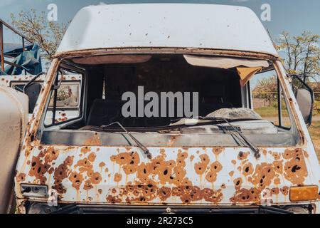 Kabine eines alten Busses (Nahaufnahme), beschädigt durch Artilleriefeuer. Krieg in der Ukraine. Russische Invasion der Ukraine. Terror der Zivilbevölkerung. Kriegsverbrechen Stockfoto