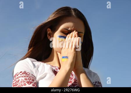 Junge ukrainische Frau mit gefalteten Händen am blauen Himmel Stockfoto