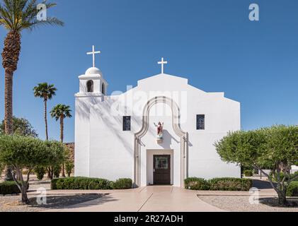 Borrego Springs, CA, USA - 24. April 2023: St. Richards Katholische Kirche weiße Fassade unter blauem Himmel mit grünem Laub Stockfoto