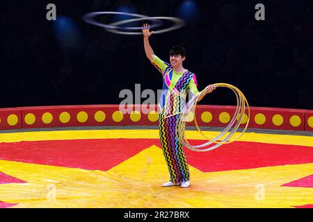 Der männliche Zirkus-Performer-Clown benutzt Hula-Hoop-Akrobatik, um die Menge zu umwerben. Stockfoto