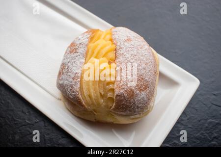 Portugiesischer Donut oder Berliner mit Eiercreme auf einem weißen Teller. Es besteht aus einem gebratenen süßen Teig gefüllt mit Sahne und Zucker. Stockfoto