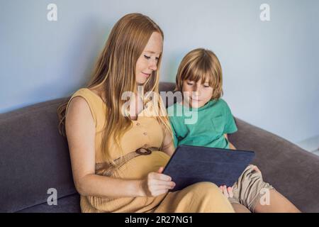 Schwangere mutter und Sohn sehen sich die Tablette an. Ein Buch lesen, einen Cartoon ansehen oder einen Videoanruf tätigen. Sehen Sie sich das Foto vom Ultraschall an Stockfoto