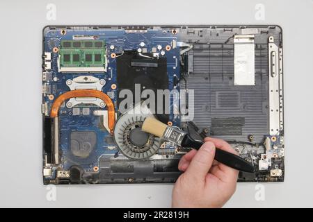 Der Techniker reinigt einen zerlegten Laptop auf weißem Hintergrund. Isoliert. Verstaubter Computer in einer Servicewerkstatt repariert. Computerplatine, Chips Stockfoto