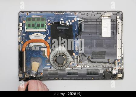 Der Techniker reinigt einen zerlegten Laptop auf weißem Hintergrund. Isoliert. Verstaubter Computer in einer Servicewerkstatt repariert. Computerplatine, Chips Stockfoto