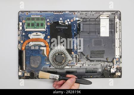 Der Techniker reinigt einen zerlegten Laptop auf weißem Hintergrund. Isoliert. Verstaubter Computer in einer Servicewerkstatt repariert. Computerplatine, Chips Stockfoto