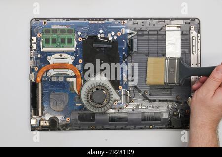 Der Techniker reinigt einen zerlegten Laptop auf weißem Hintergrund. Isoliert. Verstaubter Computer in einer Servicewerkstatt repariert. Computerplatine, Chips Stockfoto