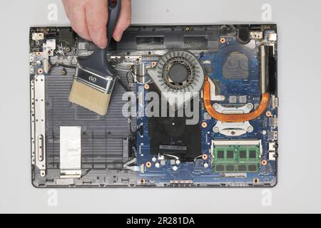 Der Techniker reinigt einen zerlegten Laptop auf weißem Hintergrund. Isoliert. Verstaubter Computer in einer Servicewerkstatt repariert. Computerplatine, Chips Stockfoto