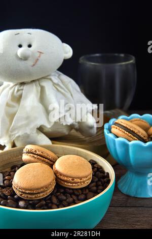 Makronen mit Kaffeegeschmack mit Kaffeebohnen und Tassen Kaffee. Ein Engel sitzt neben der Pasta. Stockfoto