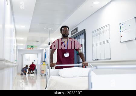 afroamerikanischer männlicher Mediziner schiebt leeres Bett im Krankenhausflur Stockfoto